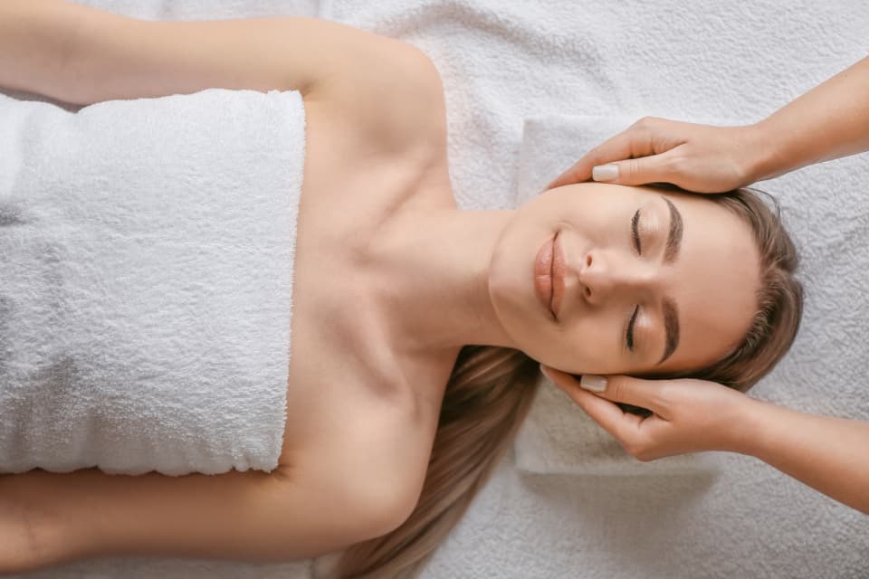 A therapist's hands at a client's temples during a facial